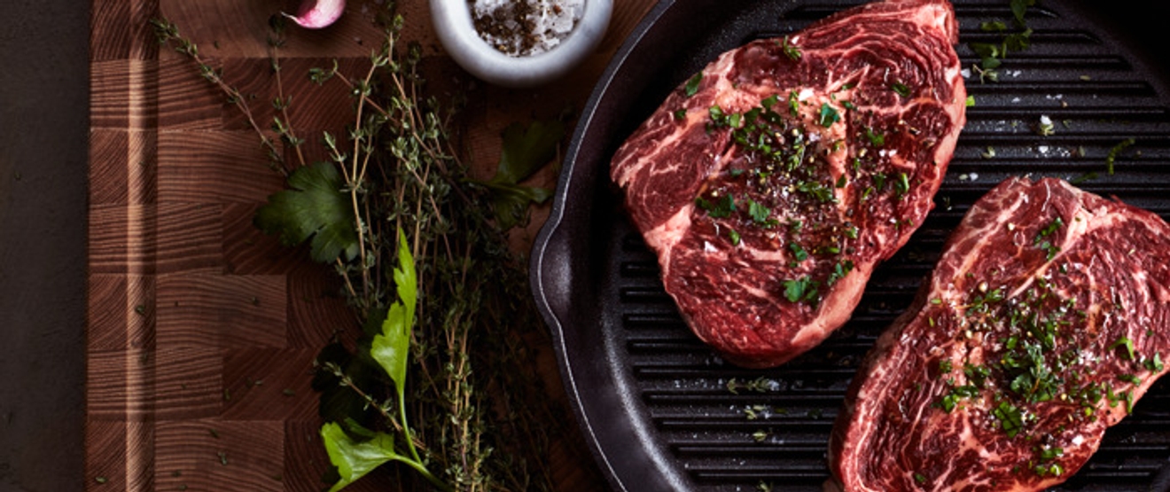 To kjøttstykker i en støpejernspanne med en krydderkvist ved siden av