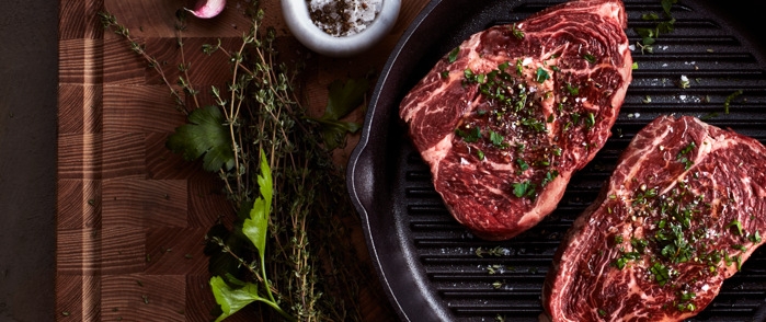 To kjøttstykker i en støpejernspanne med en krydderkvist ved siden av