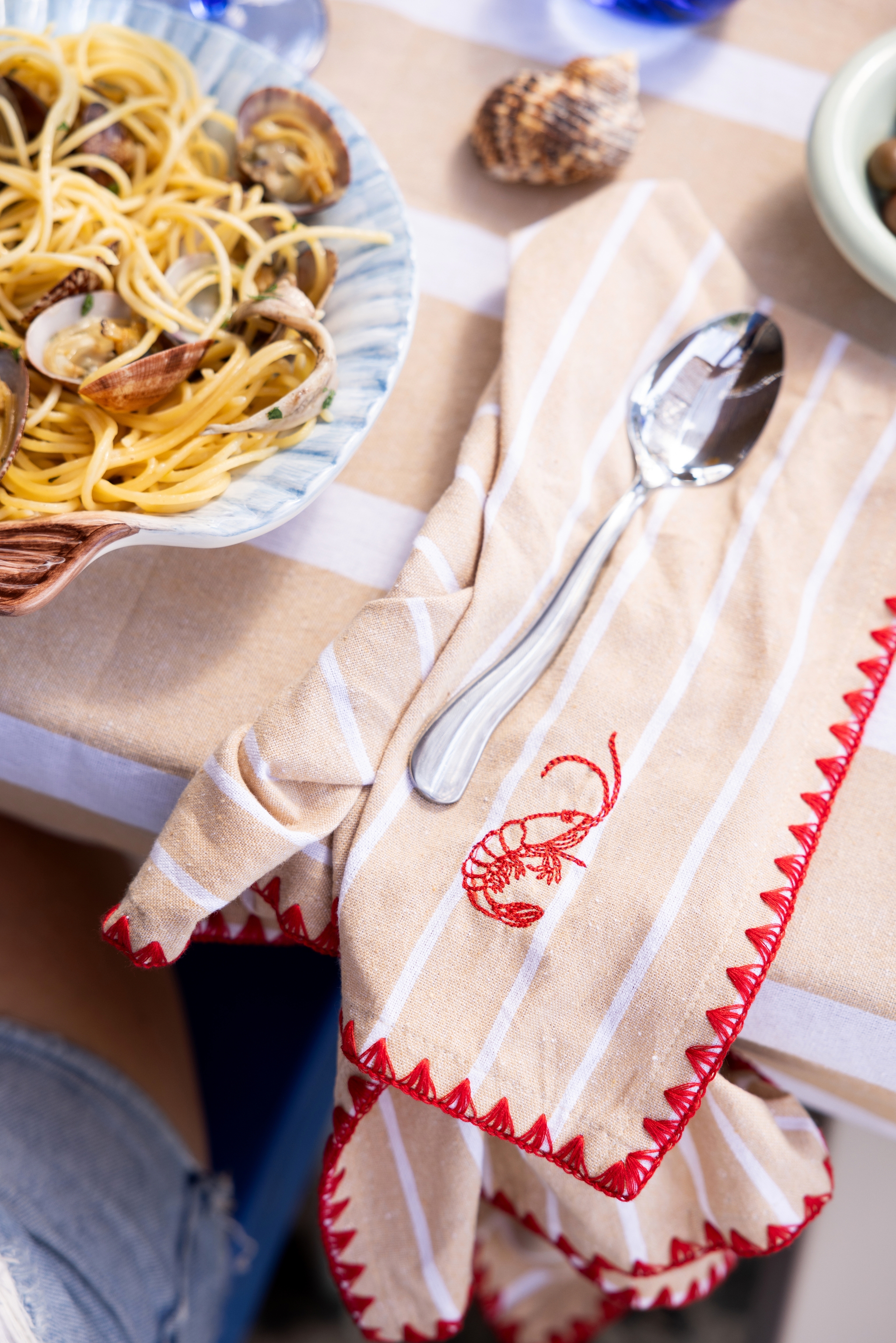 Närbild på en tallrik spaghetti med musslor på dukat bord med randig servett och sked.