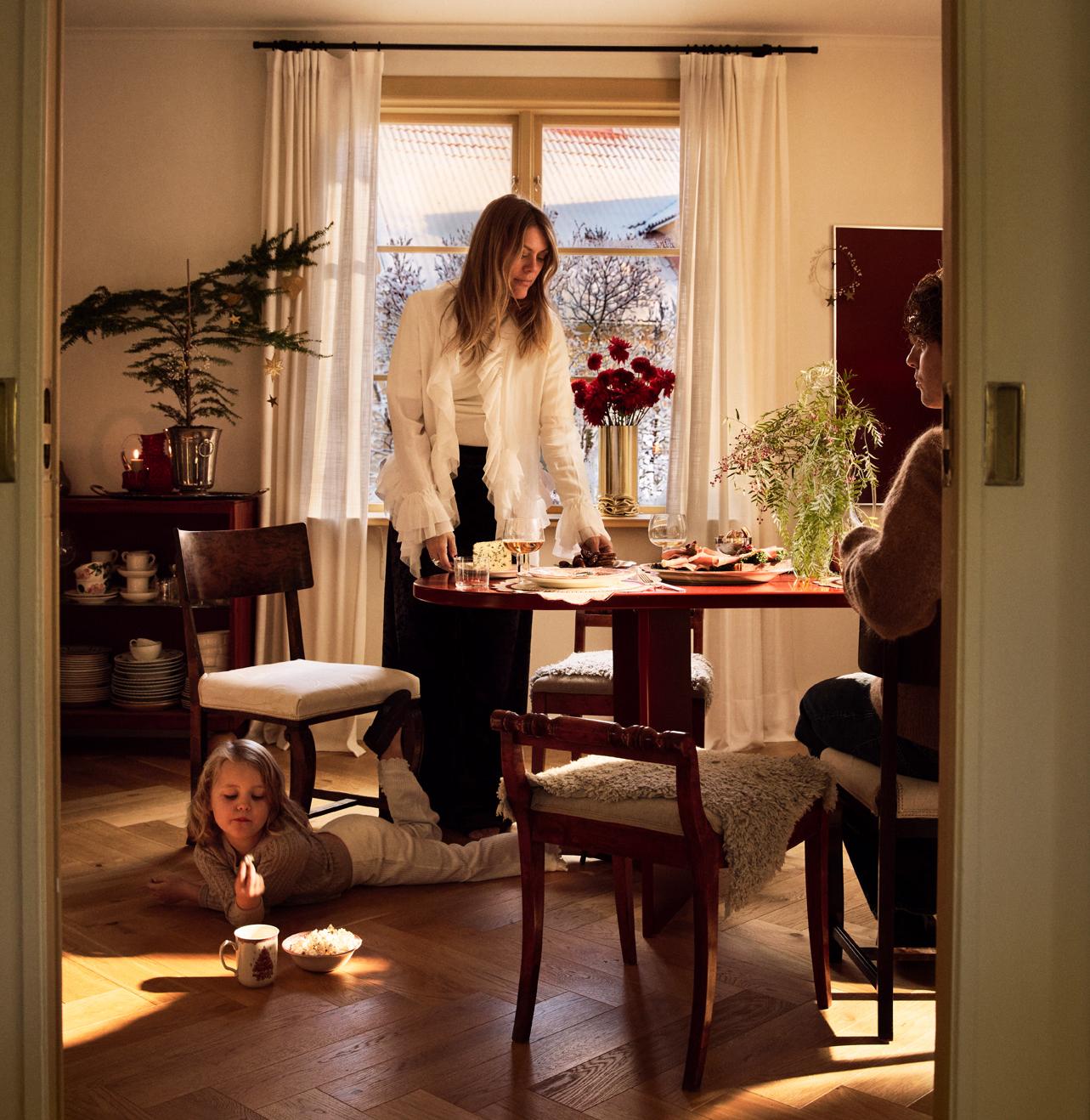 Familj samlas kring ett juldukat bord i ett varmt och solbelyst vardagsrum.