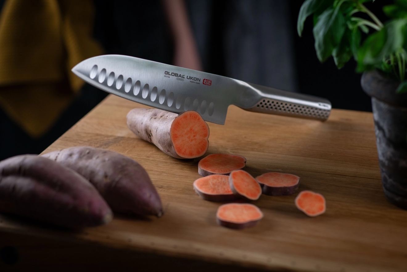Global Ukon keittiöveitsi jolla leikataan bataattia puisella leikkuulaudalla 
