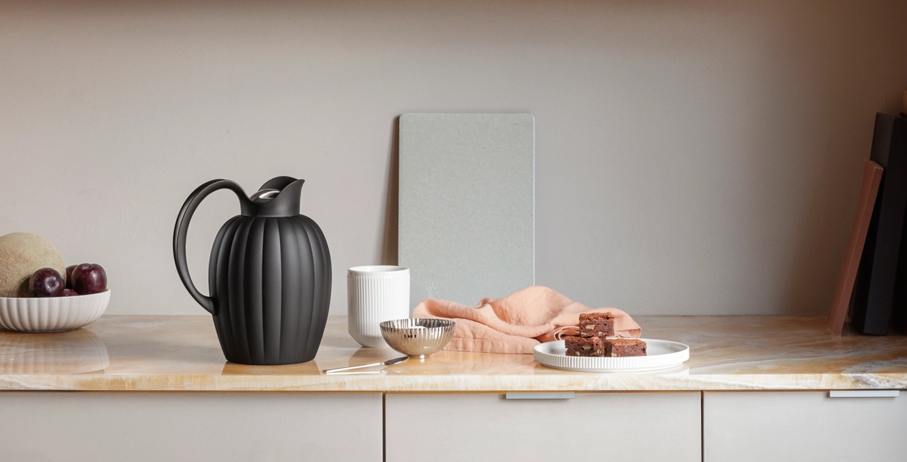 Modern köksbänk och trähylla inredd med räfflade kannor, frukt, brownies, böcker och minimalistisk köksutrustning.