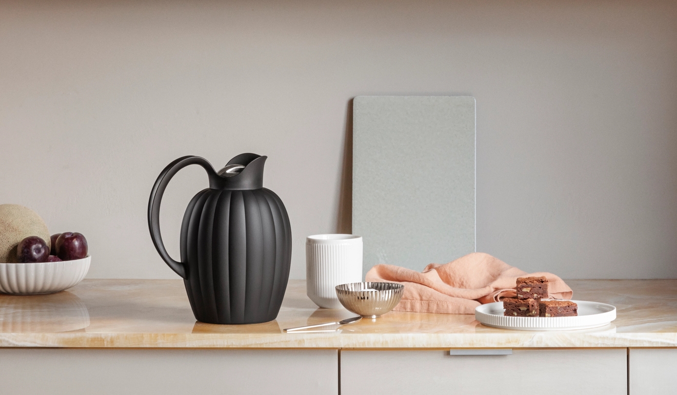 Modern köksbänk och trähylla inredd med räfflade kannor, frukt, brownies, böcker och minimalistisk köksutrustning.