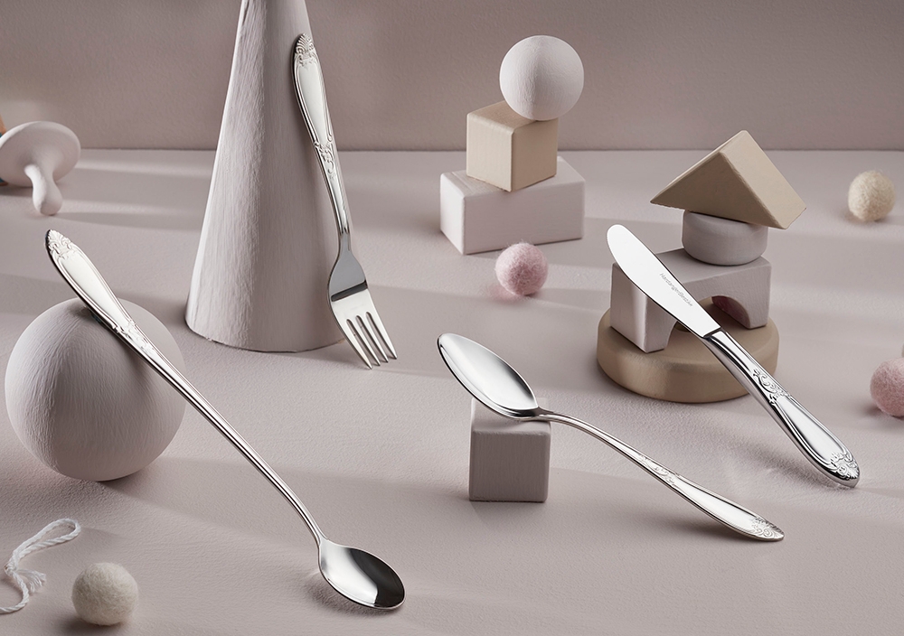 Bestikksett i sølv med dekorative håndtak, inkludert skjeer, gaffel og kniv, plassert på en lys overflate med minimalistisk dekor.