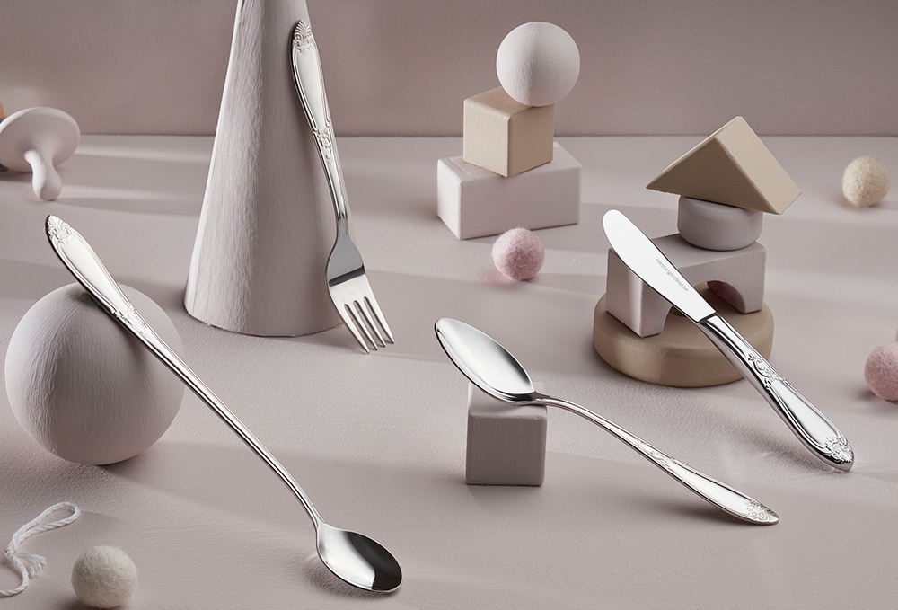 Bestikksett i sølv med dekorative håndtak, inkludert skjeer, gaffel og kniv, plassert på en lys overflate med minimalistisk dekor.