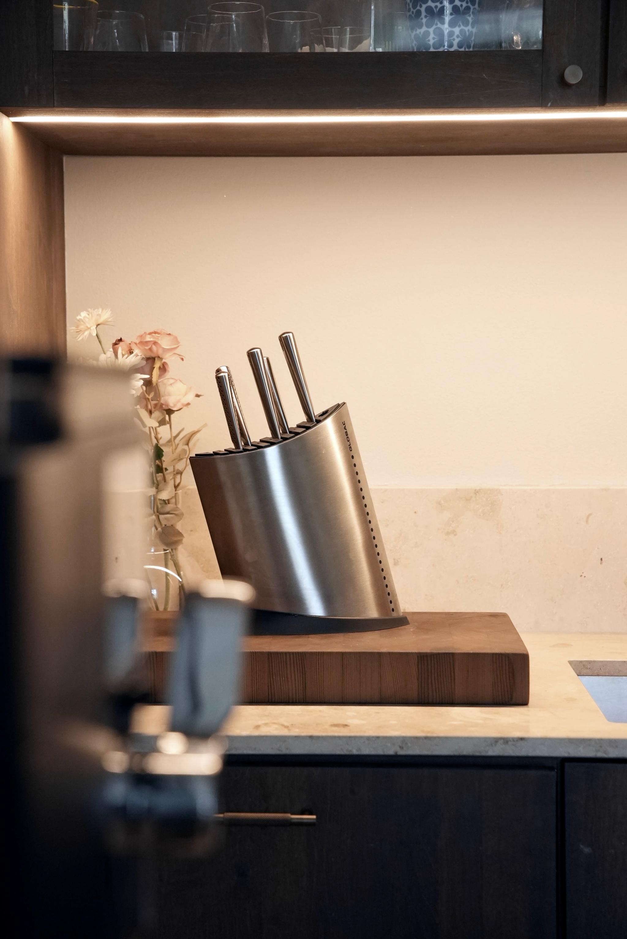 Modern knivblock i rostfritt stål står på en träskärbräda i ett stilrent kök.