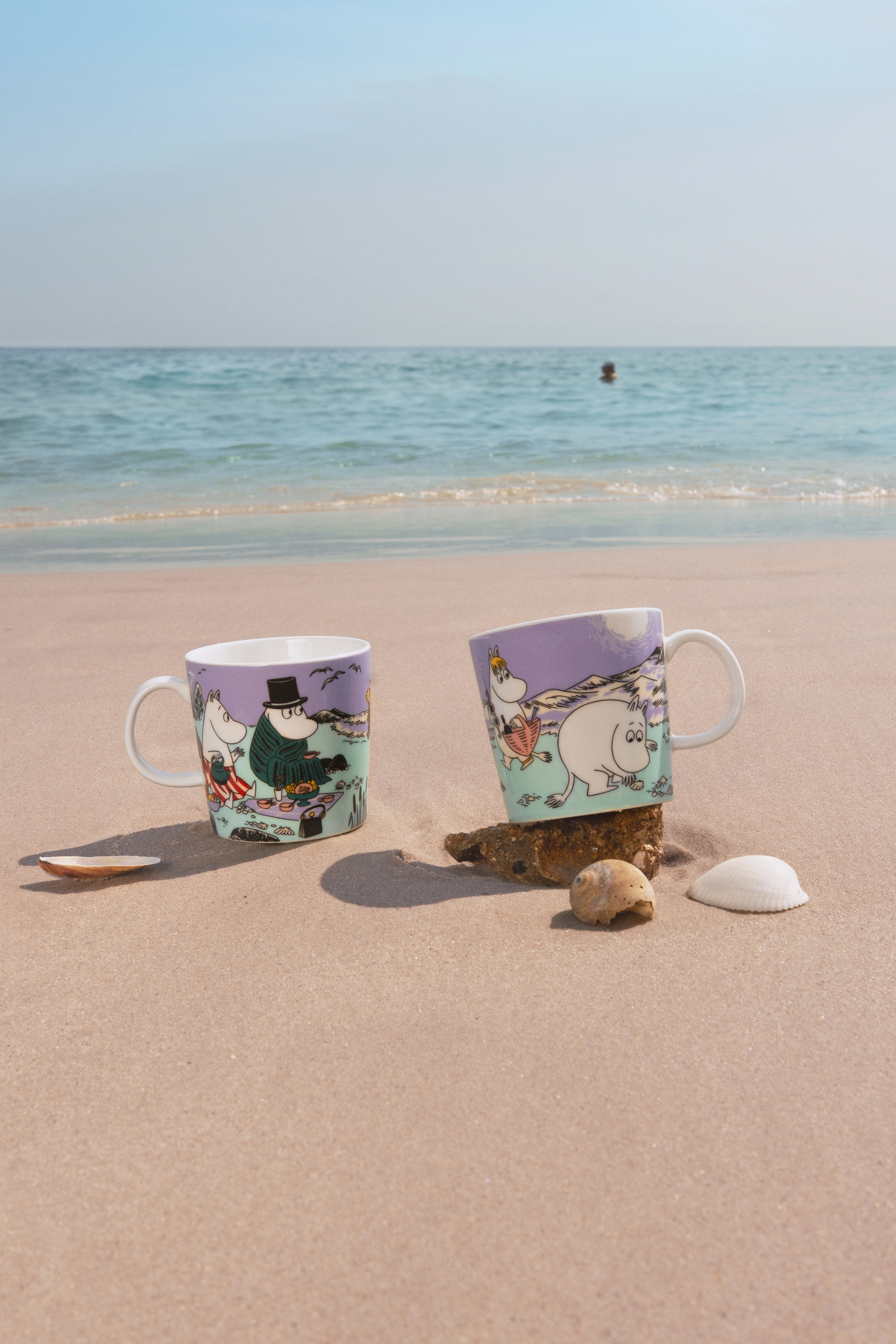 two mugs are sitting on a sandy beach near the ocean