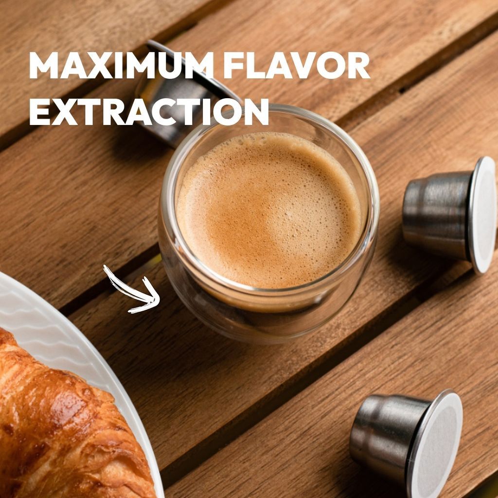 A cup of espresso, reusable coffee capsules, and a croissant on a wooden table. Text: MAXIMUM FLAVOR EXTRACTION.