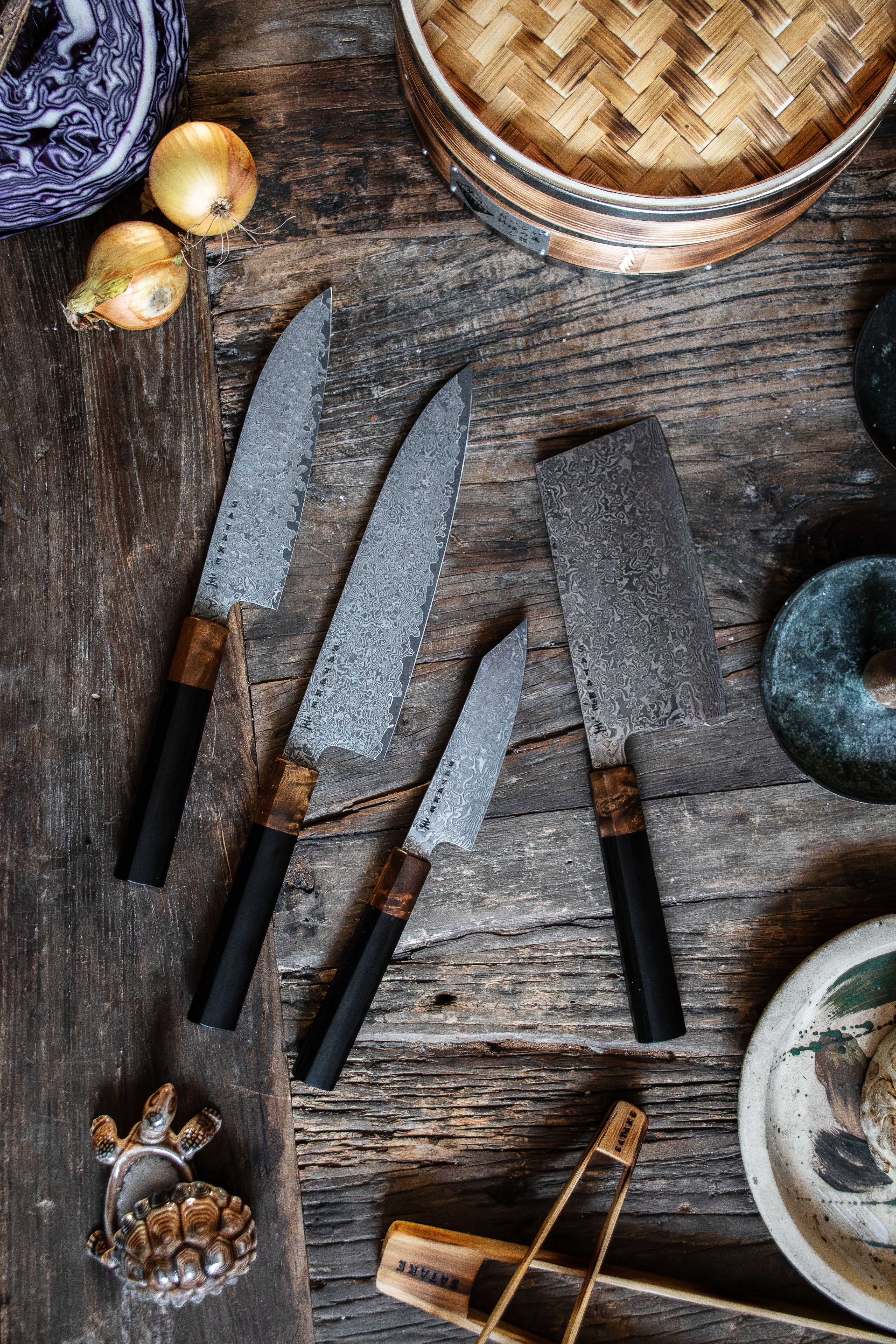 Ett set med fyra damaskusstålknivar med svarta och trähandtag på en rustik träyta