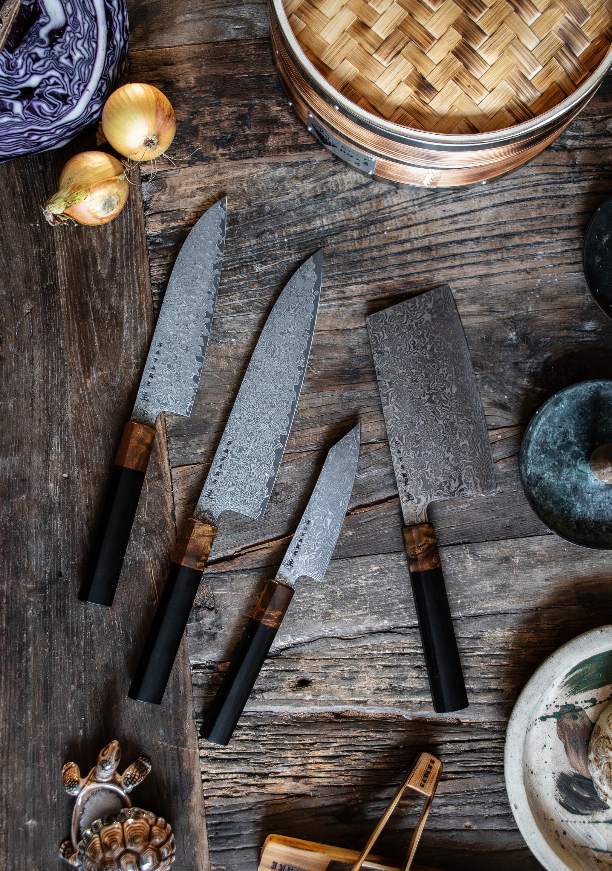 Ett set med fyra damaskusstålknivar med svarta och trähandtag på en rustik träyta