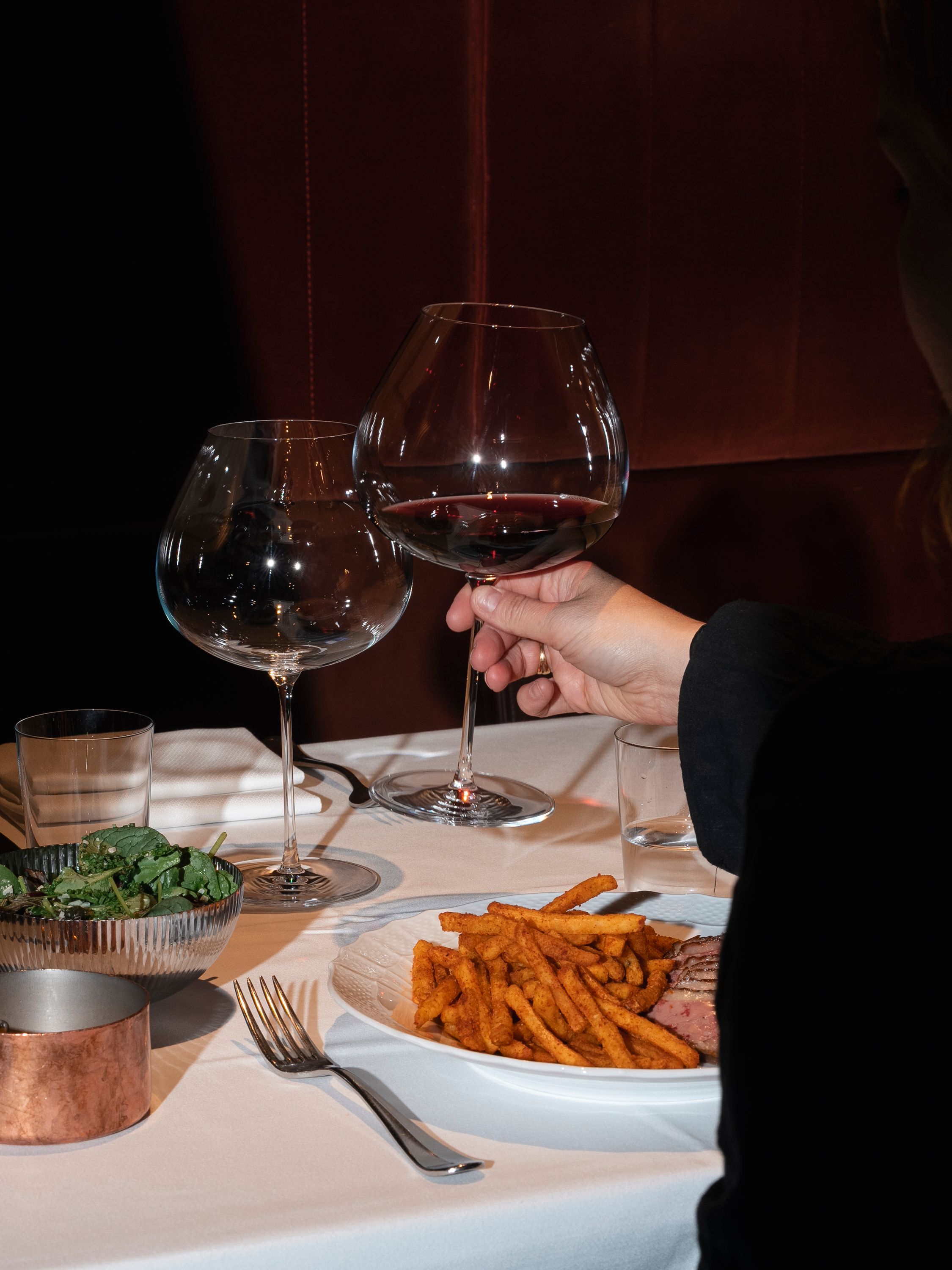 En person är på väg att dricka ur ett glas rödvin vid ett restaurangbord