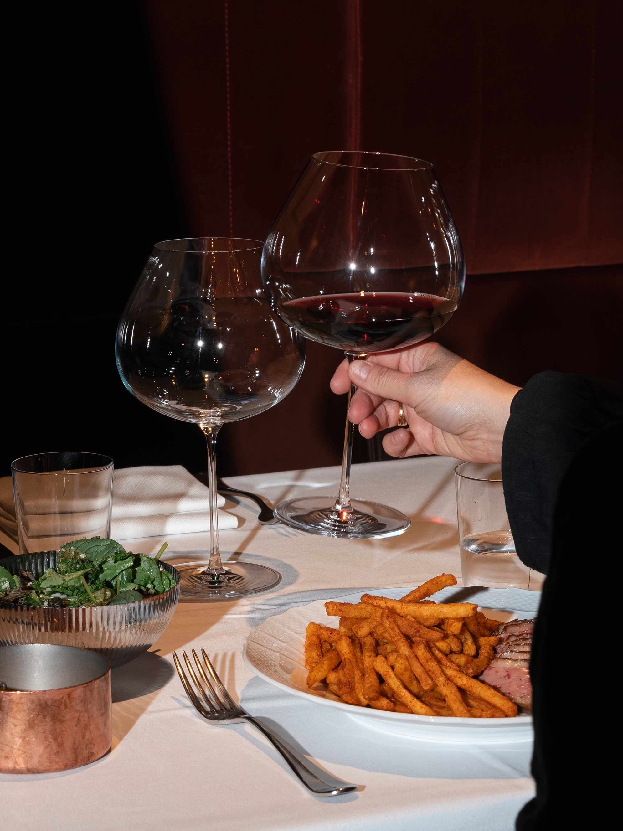 En person är på väg att dricka ur ett glas rödvin vid ett restaurangbord