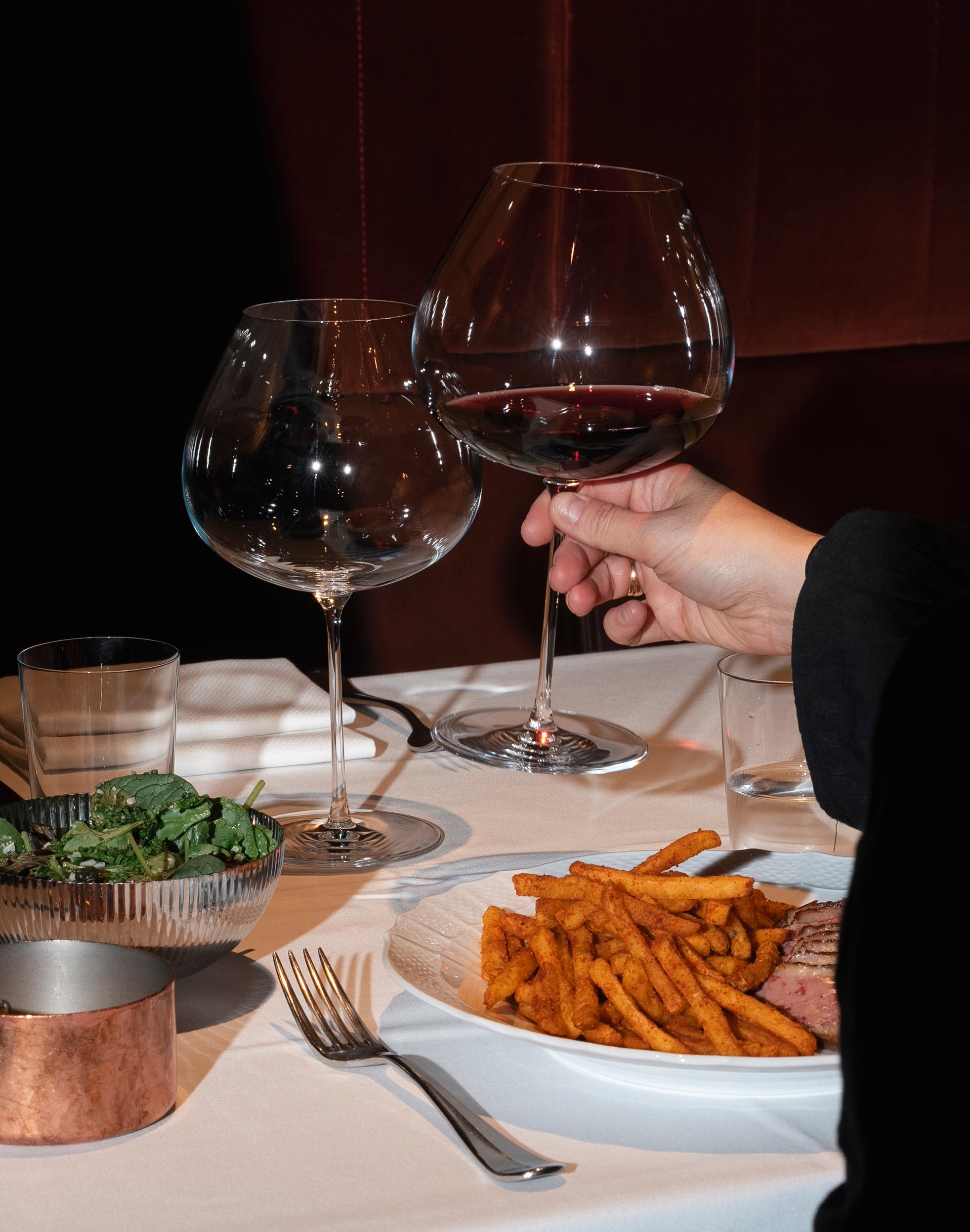 En person är på väg att dricka ur ett glas rödvin vid ett restaurangbord