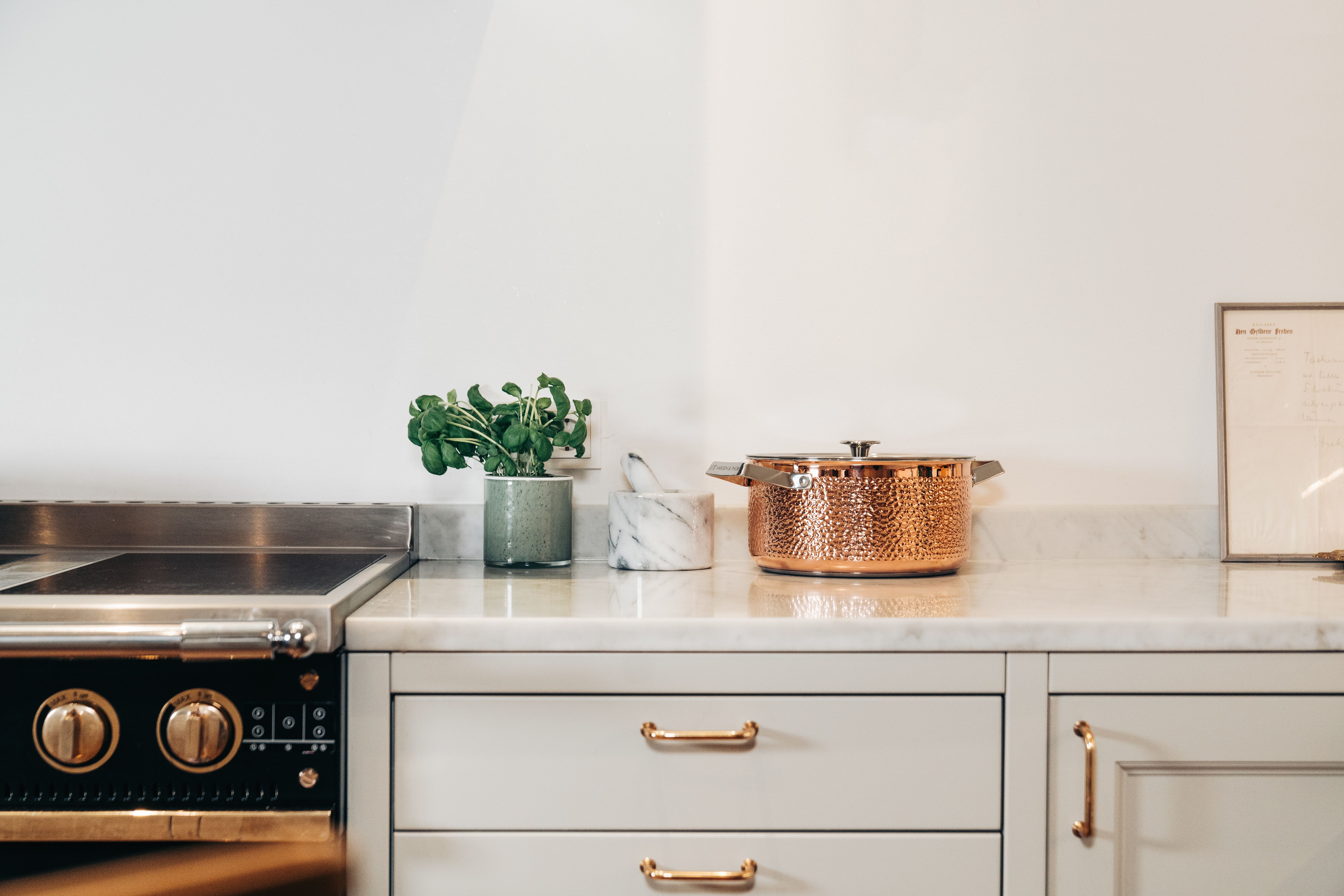 Köksbänk med svart spis, en gryta i hamrat koppar och krukväxt.