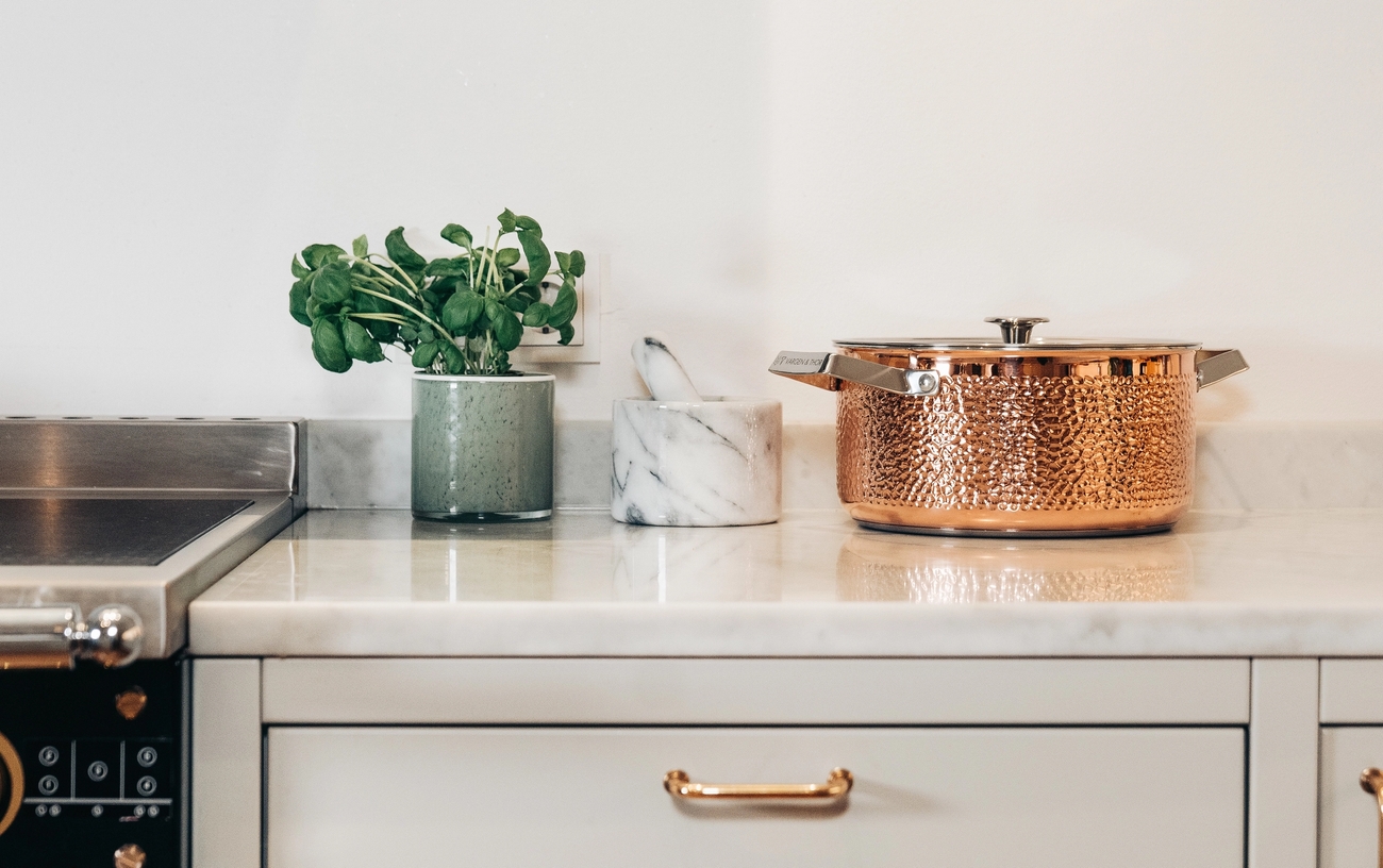 Köksbänk med svart spis, en gryta i hamrat koppar och krukväxt.