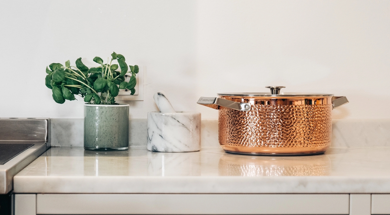 Köksbänk med svart spis, en gryta i hamrat koppar och krukväxt.