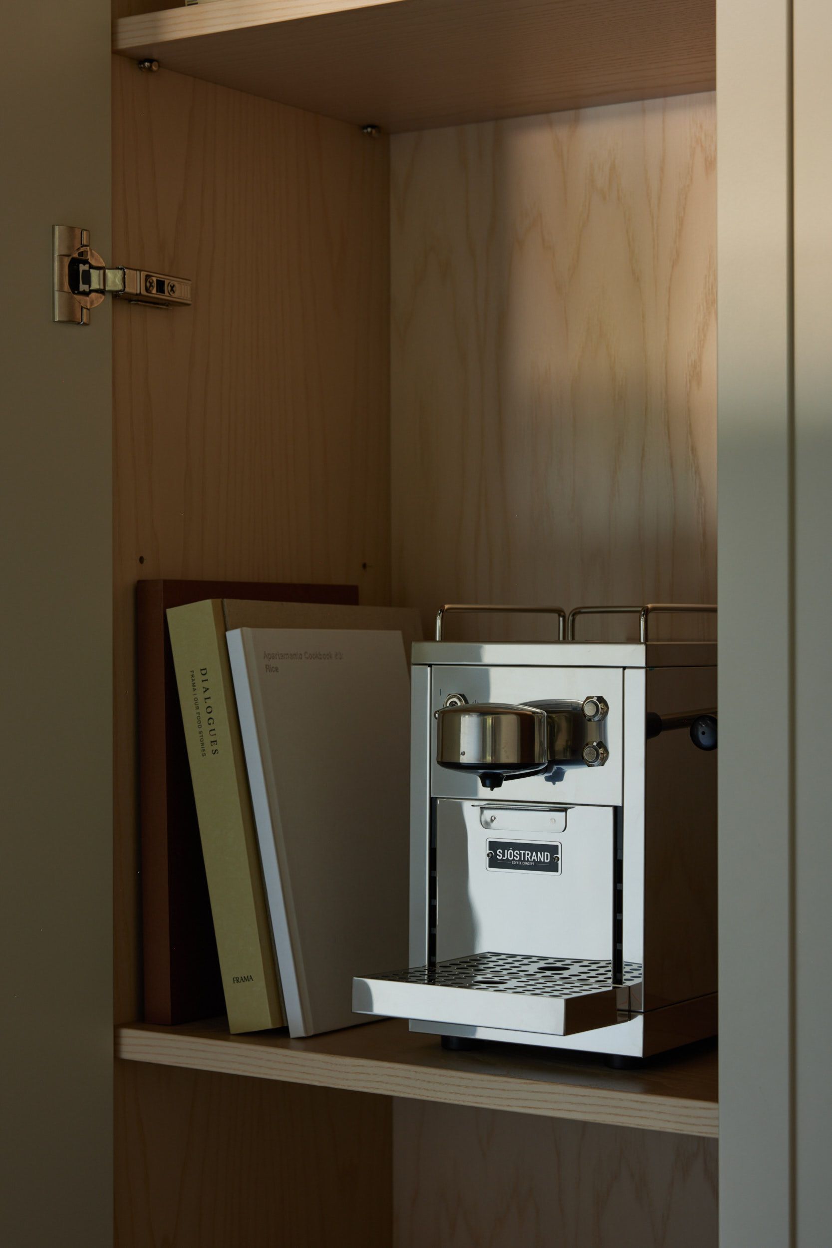 A Sjostrand stainless steel coffee machine and books on a light wood shelf.