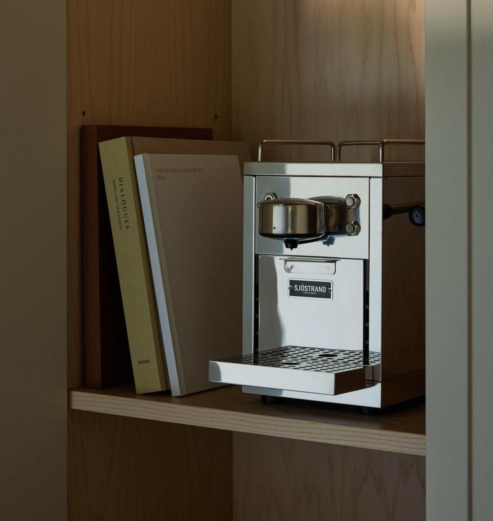 A Sjostrand stainless steel coffee machine and books on a light wood shelf.