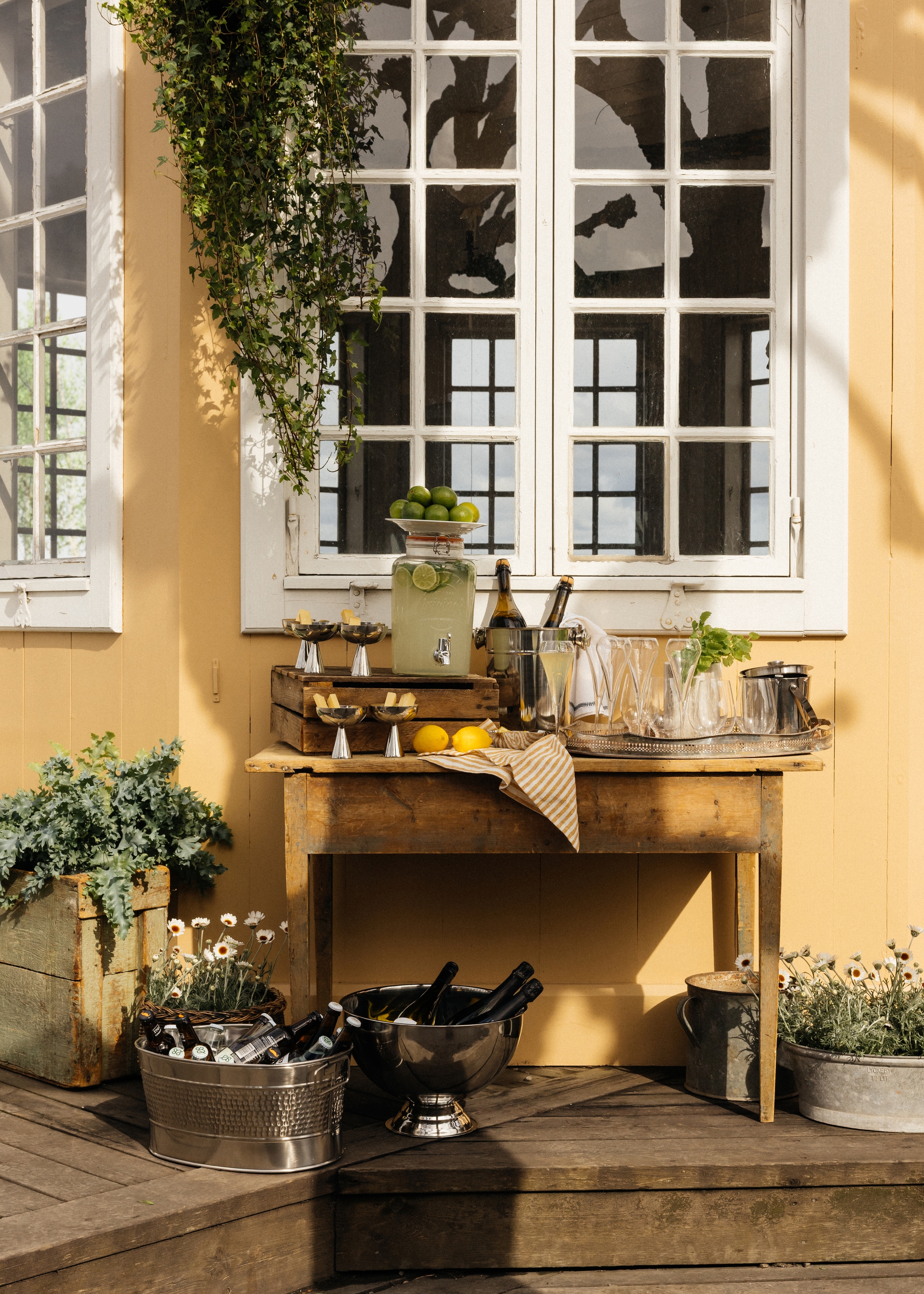 Bar utomhus på ett träbord med ölhink, glas, lemonad i tappkran mot en gult hus