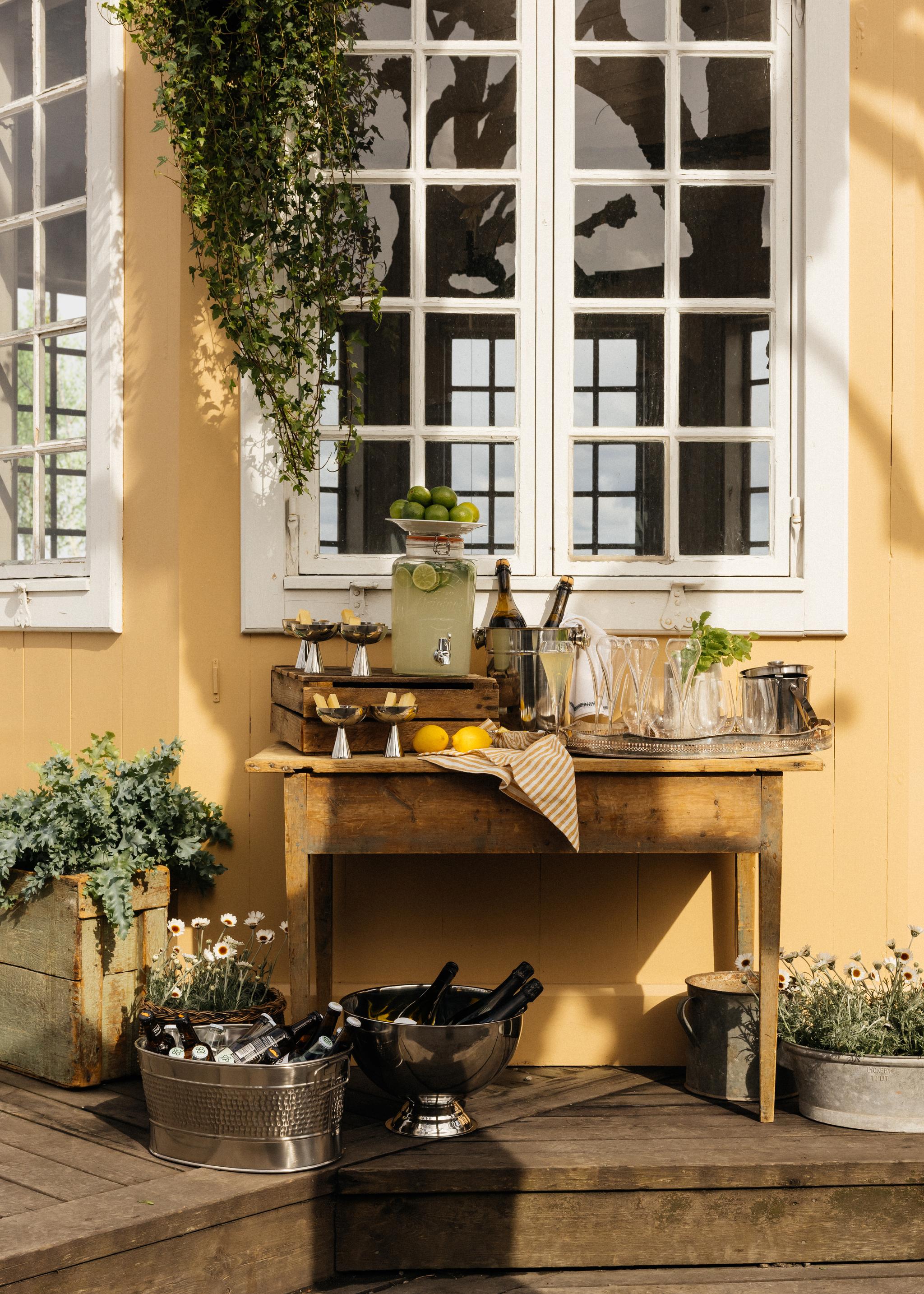 Bar utomhus på ett träbord med ölhink, glas, lemonad i tappkran mot en gult hus