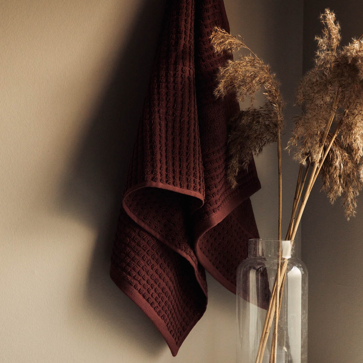 Vinröd handduk som hänger på en krok mot en beige vägg