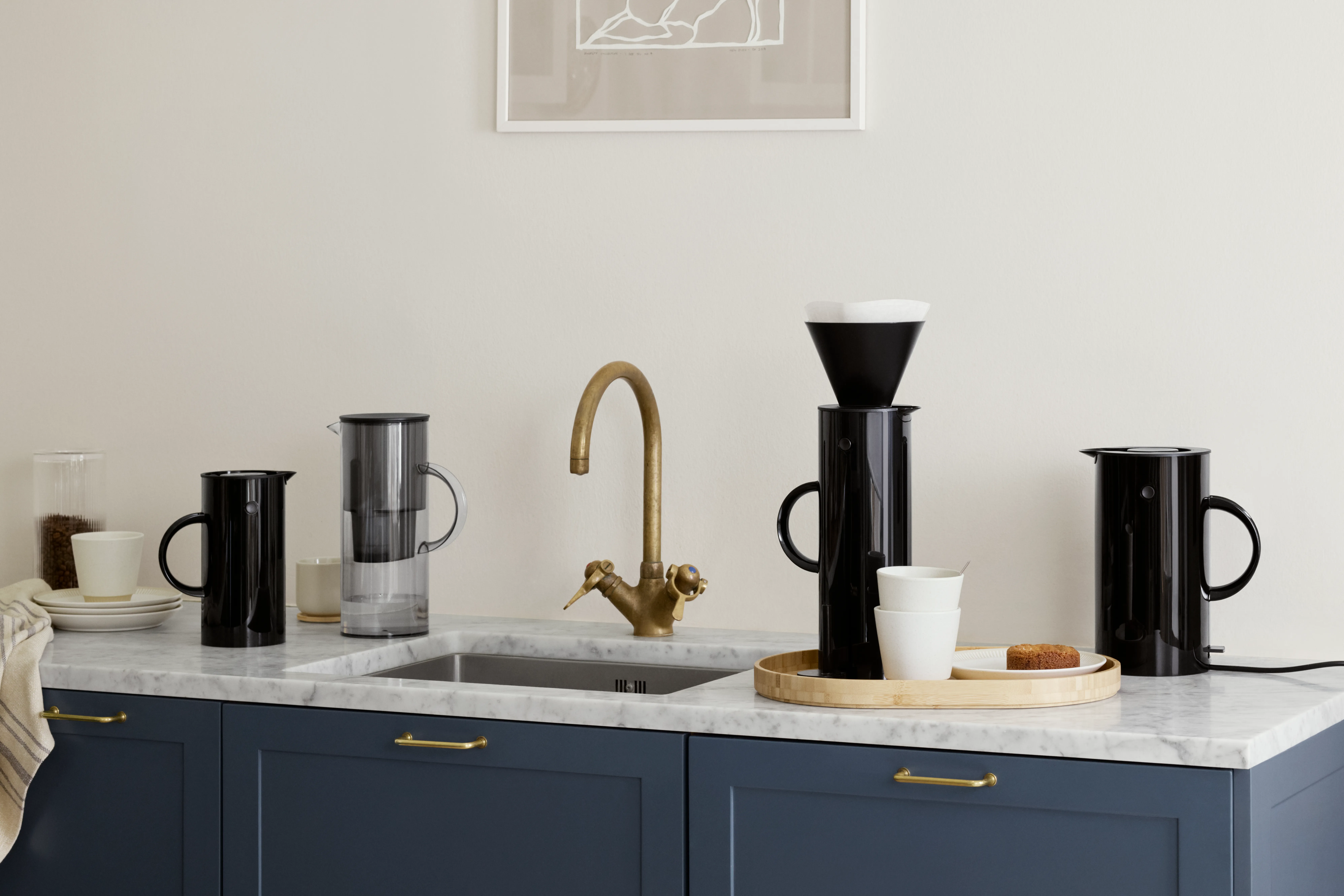 Moderne kjøkkenbenk med utstyr for svart kaffe, en vannfilterkanne og en messingkran.