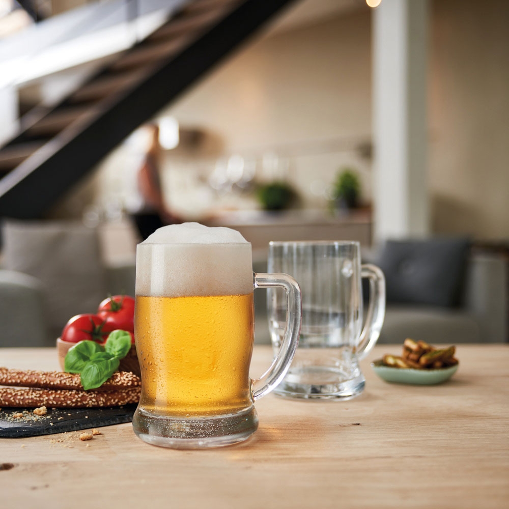 Ölglas med skummande öl och ett tomt glas på ett träbord bredvid grissini, tomater och basilika
