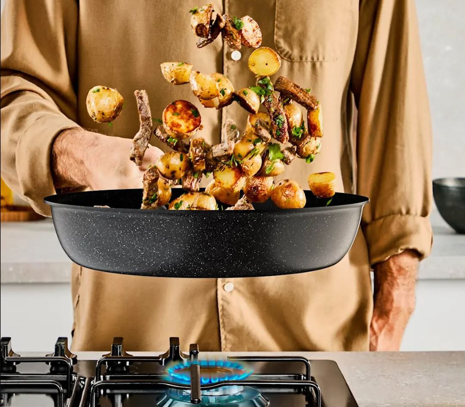 a man is cooking potatoes in a frying pan on a stove .