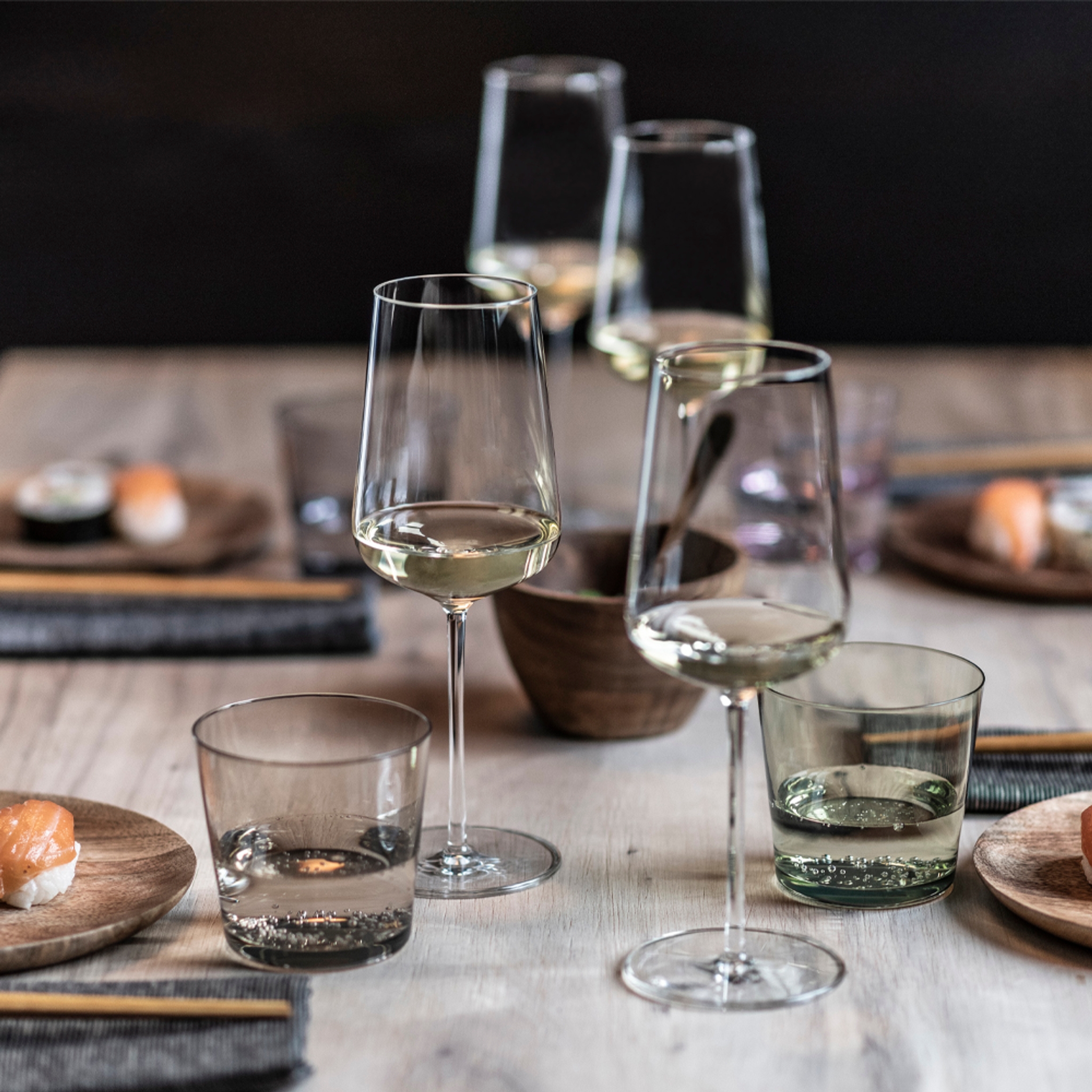 Et lyst trebord dekket med glass hvitvin, vann, sushi og spisepinner.