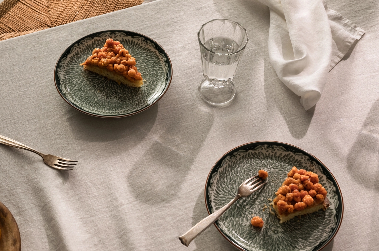 Omenapiirakka vihreillä kuviollisilla lautasilla seisomassa pöydällä, jossa on beige pellavainen pöytäliina