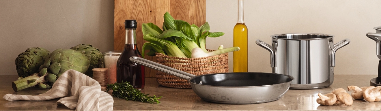 Keramiska stekpannor i svart och vitt med grönsaker i på träbänk