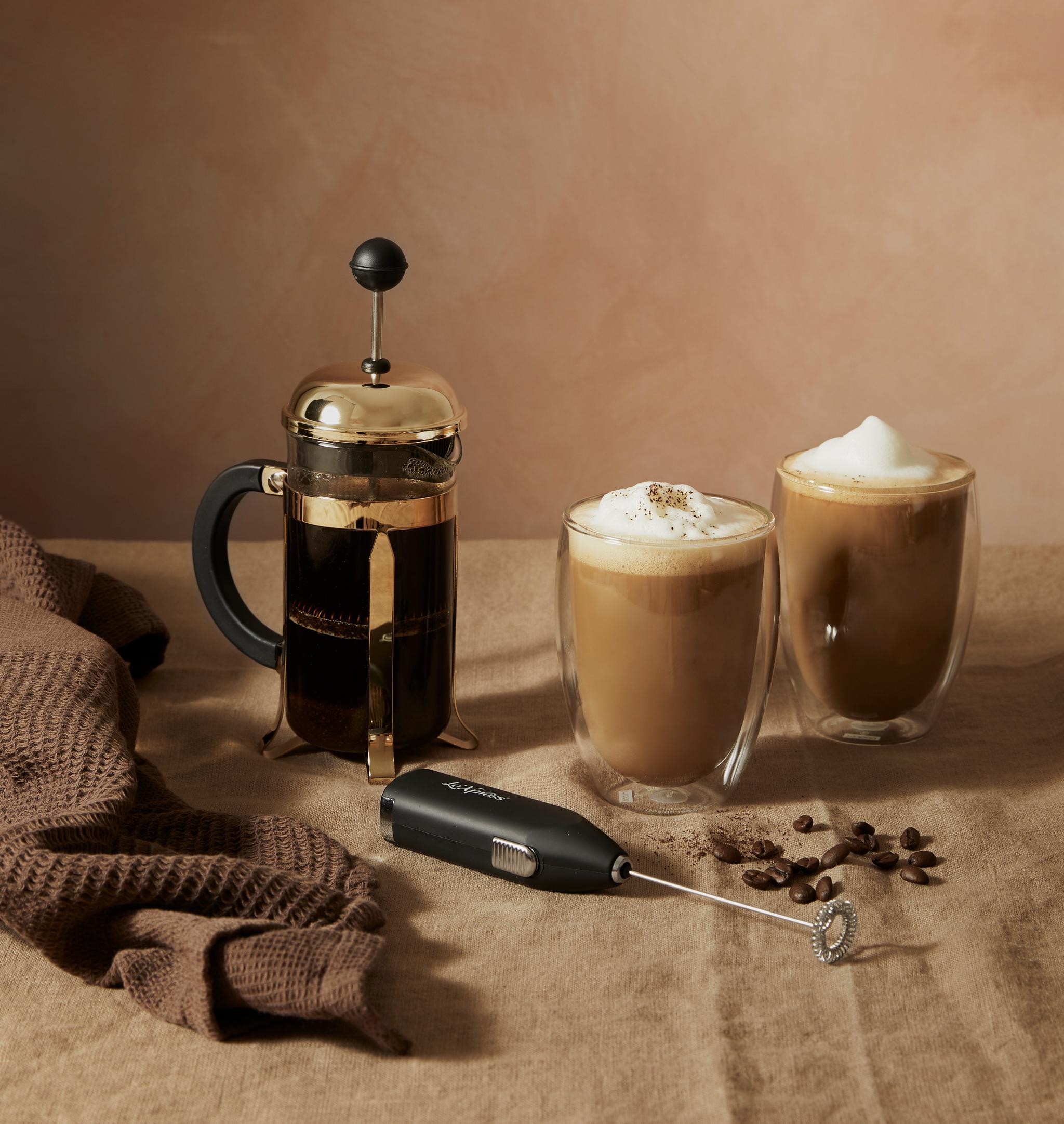 En kaffepresse, to glass kaffe og en melkeskummer på et bord