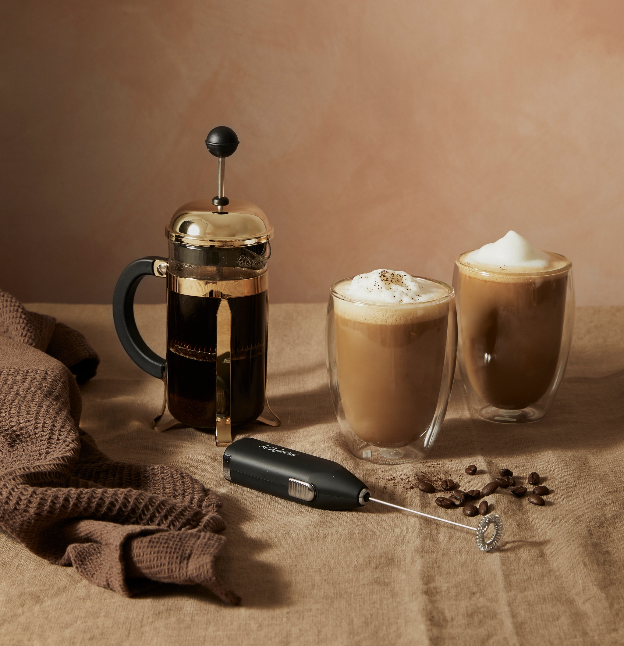 En kaffepresse, to glass kaffe og en melkeskummer på et bord