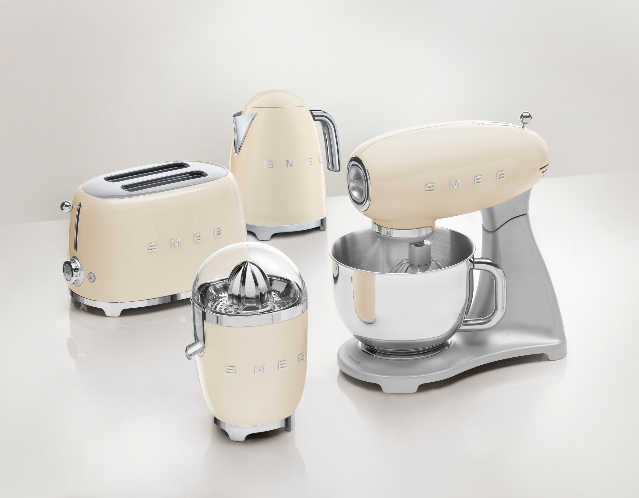 Vaaleanbeige Smeg-keittiökoneiden setti, johon kuuluu yleiskone, leivänpaahdin, vedenkeitin ja sitruspuristin, valkoisella taustalla.