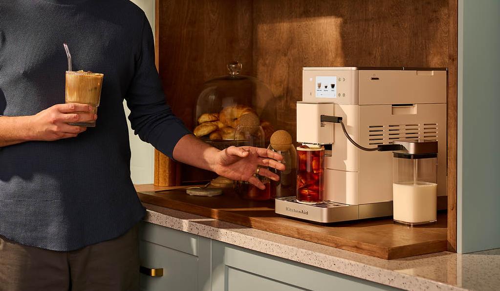 Leende man gör en iskaffe med en modern kaffemaskin i ett stilrent kök.