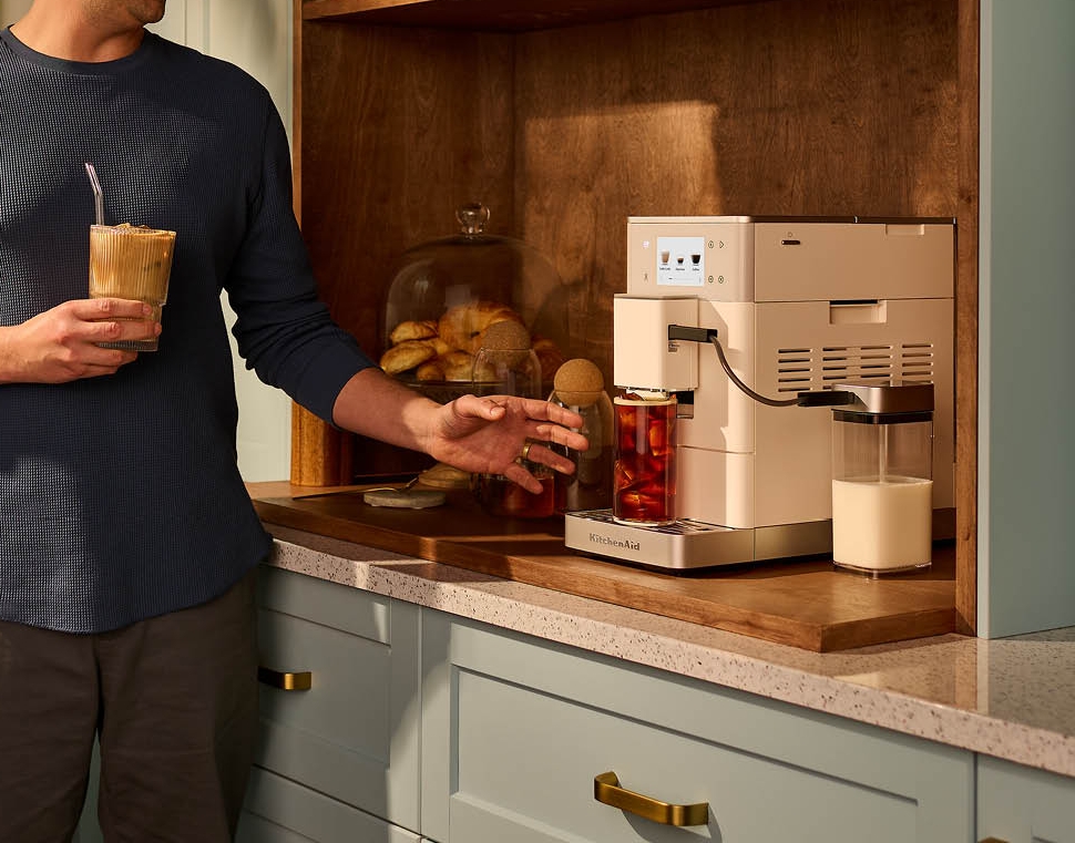 Leende man gör iskaffe med en modern kaffemaskin i ett stilrent kök.