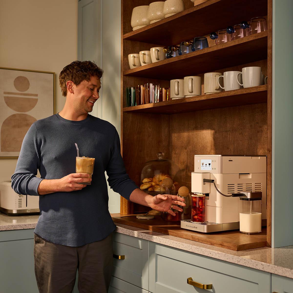 Leende man gör en iskaffe med en modern espressomaskin i ett stilrent kök.