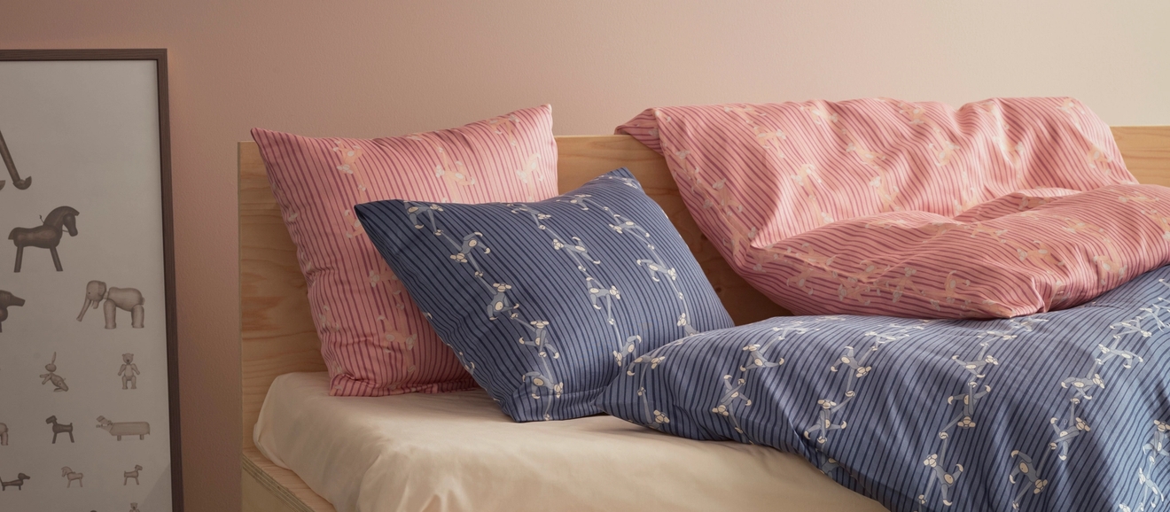 Barnrum med en säng med blått täcke och rosa och blå kudar. en tavla med olika djur står bredvid sängen