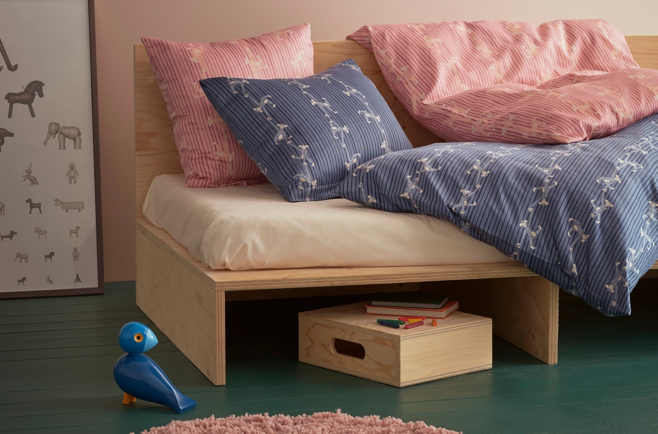 Barnrum med en säng med blått täcke och rosa och blå kundar. en tavla med olika djur står bredvid sängen