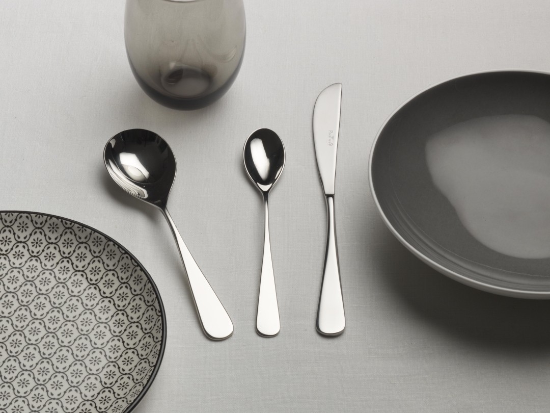 a table topped with plates , spoons , knives and glasses .