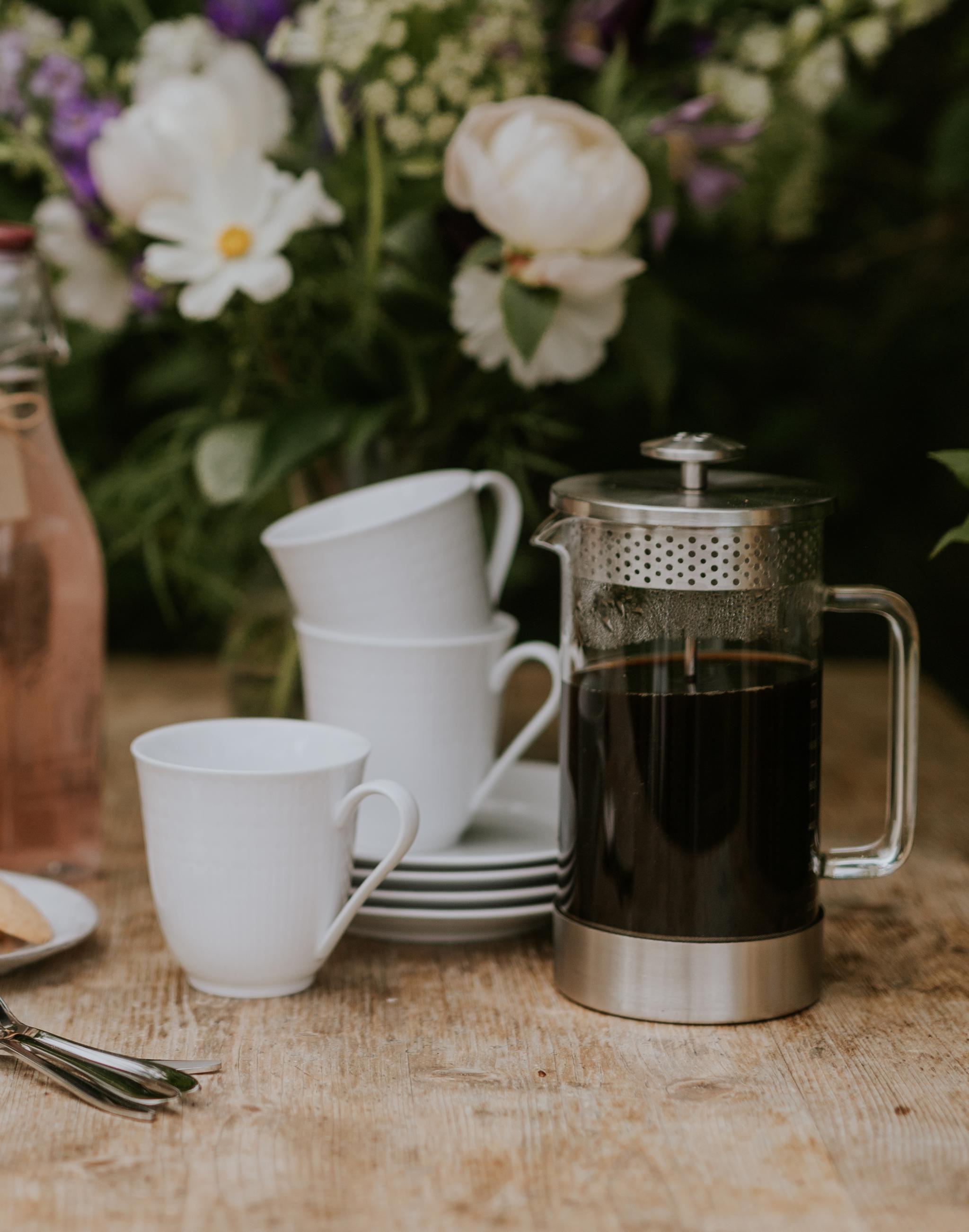 Kaffepress med kaffe och koppar på ett träbord utomhus