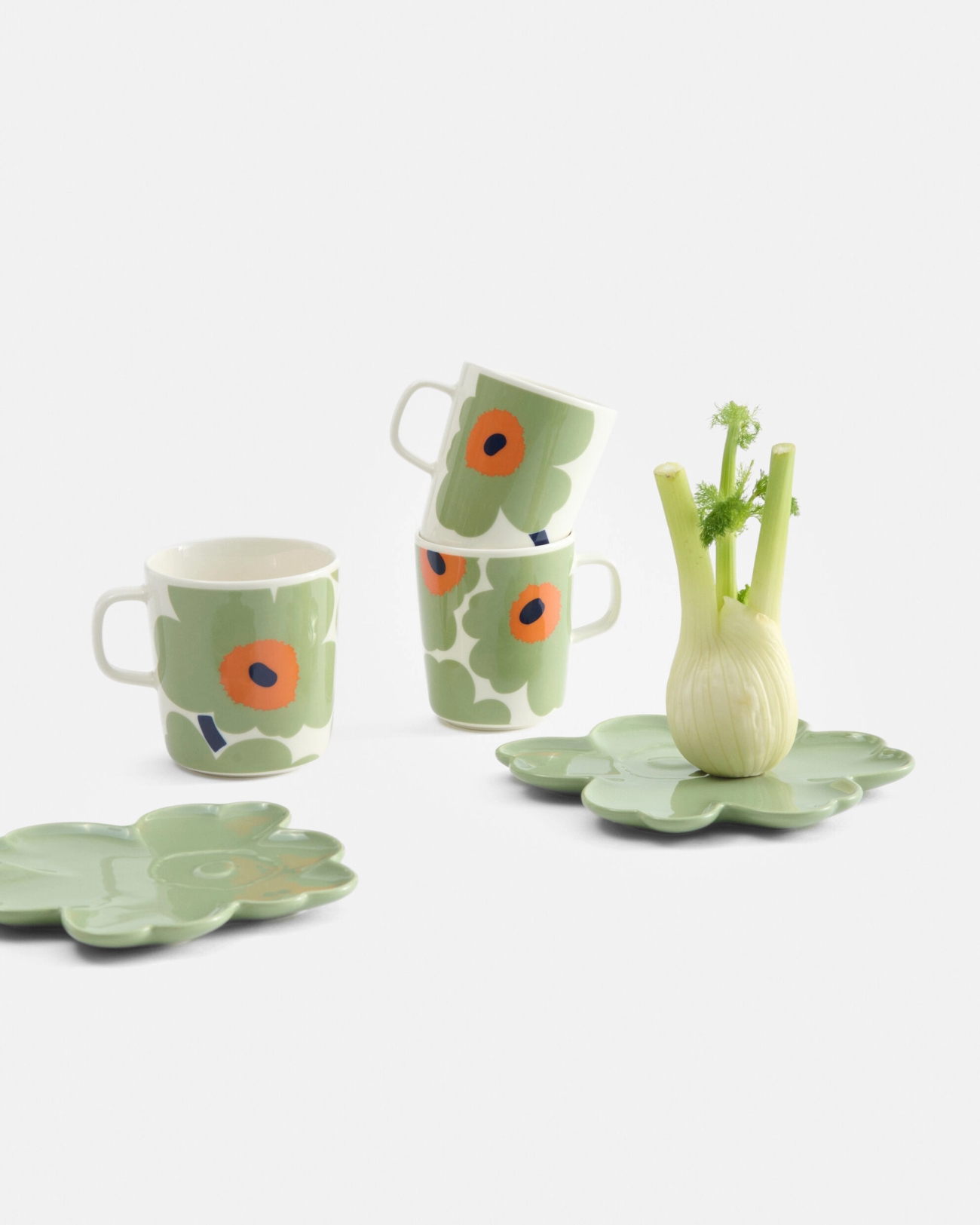 Green mugs with orange floral patterns, matching green flower plates, and a fennel bulb.