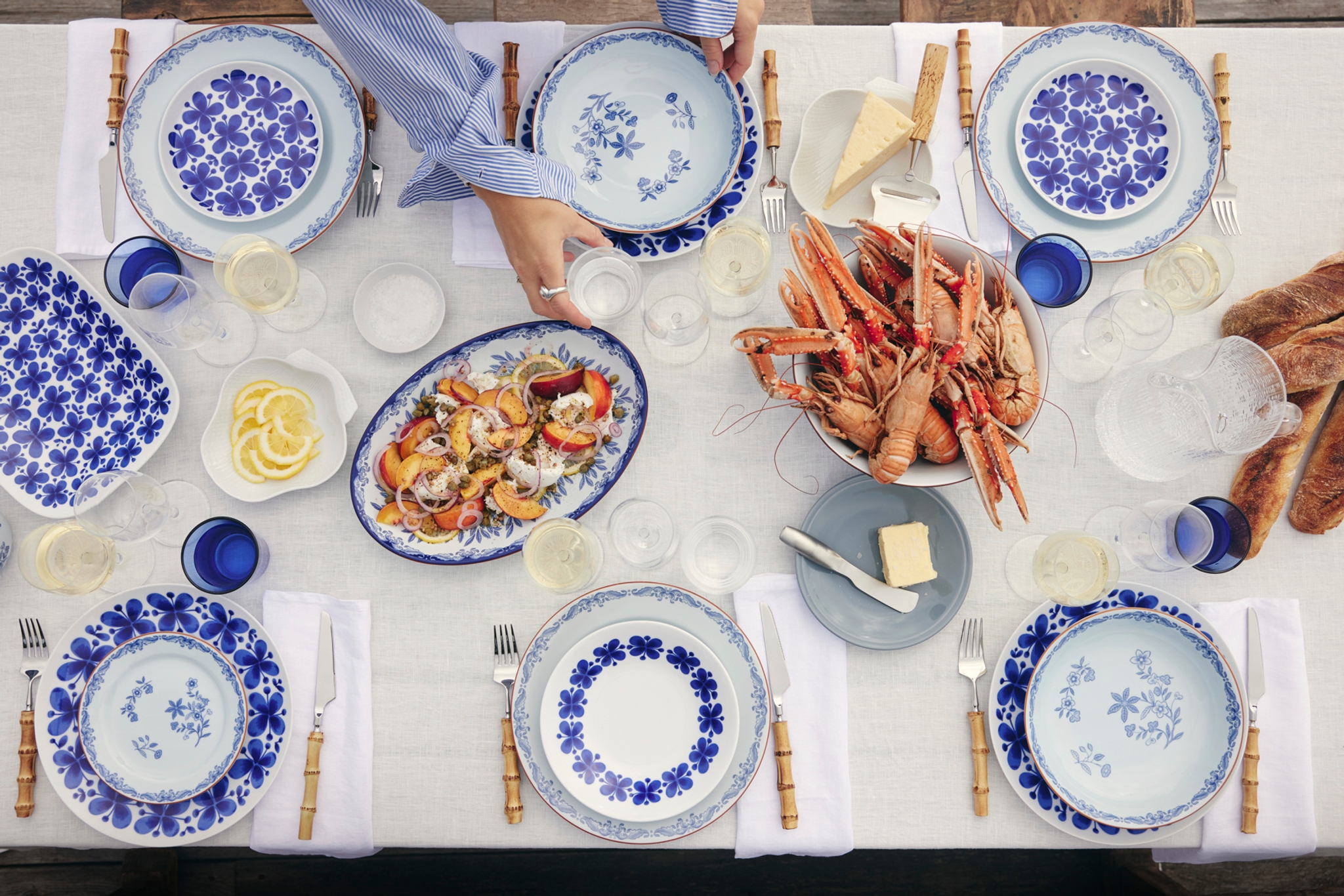 Sommerlig dekket bord med blåmønstret servise, sjømat, ferskt brød og hvitvin klart for et hyggelig måltid utendørs.