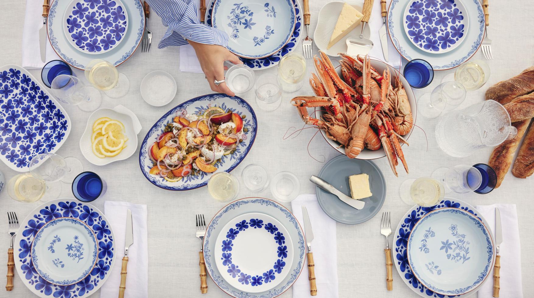 Sommerlig dekket bord med blåmønstret servise, sjømat, ferskt brød og hvitvin klart for skalldyrmåltid utendørs.