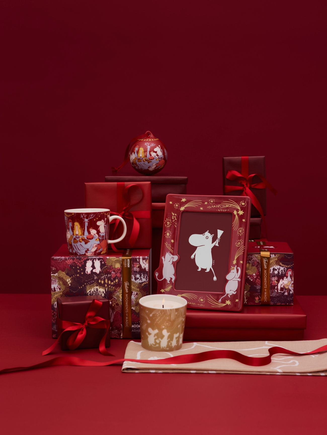 Festive Moomin-themed gifts in red and gold, including a mug, ornament, photo frame, candle, and wrapped boxes.