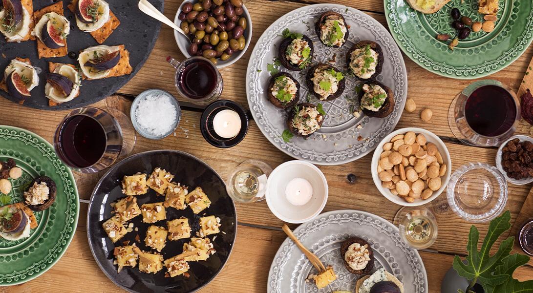 Runsas tapas- ja juustopöytä viikunoineen, oliiveineen ja viinilaseineen puisella pöydällä.