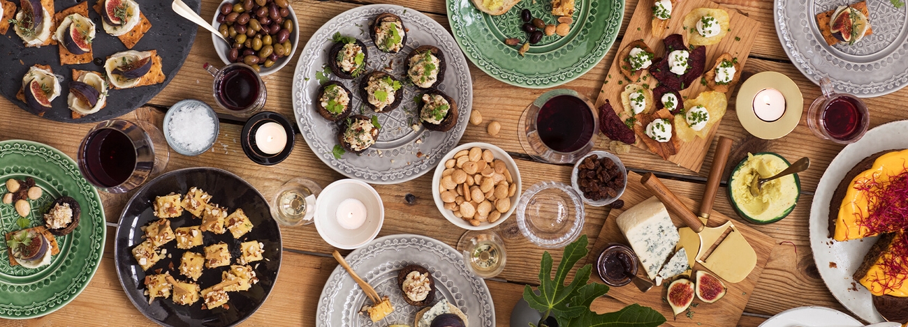 Ett bord dukas med många olika tapsasrätter upplagda på olika fat, tallrikar och skärbrädor