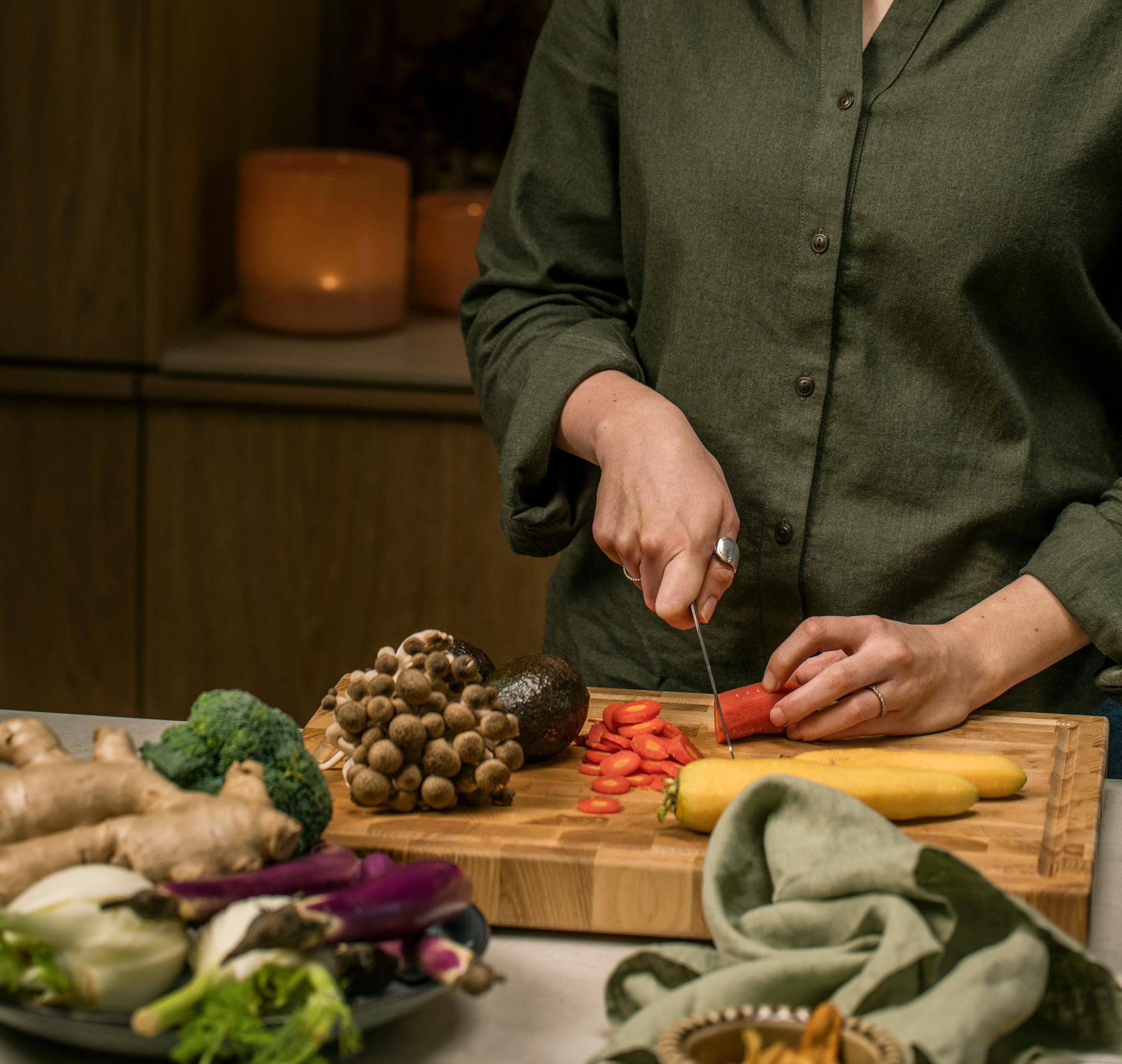 En kvinna står och skär grönsaker på en skärbräda av trä