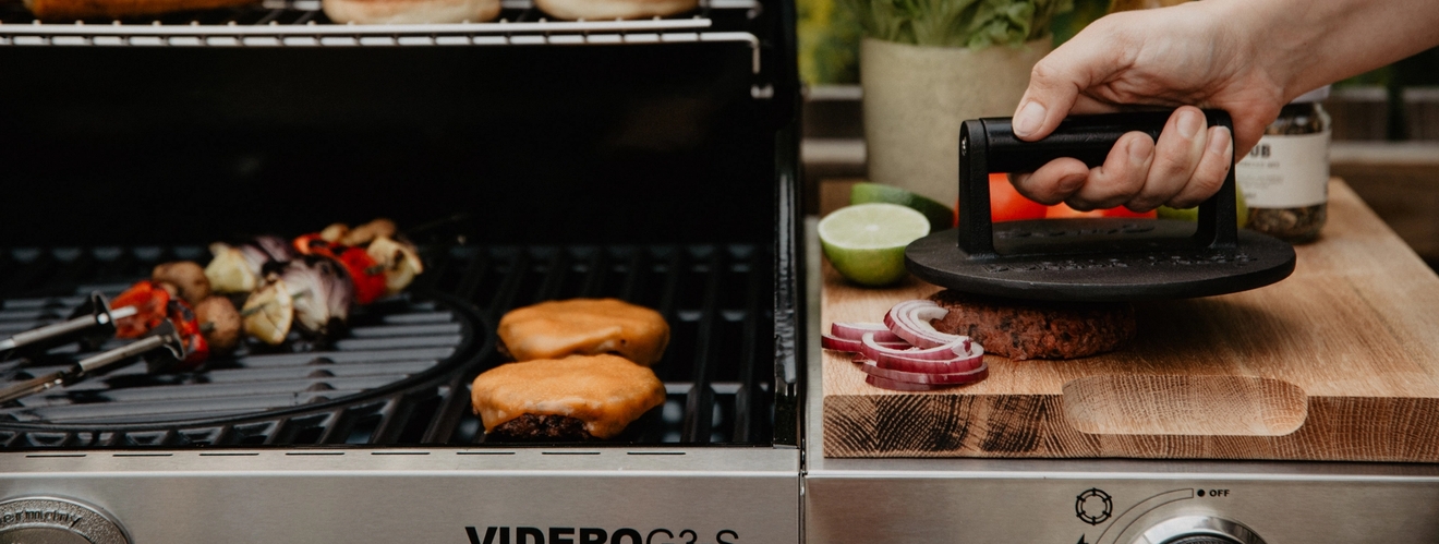 Hamburgerpress på stekbord vid grill