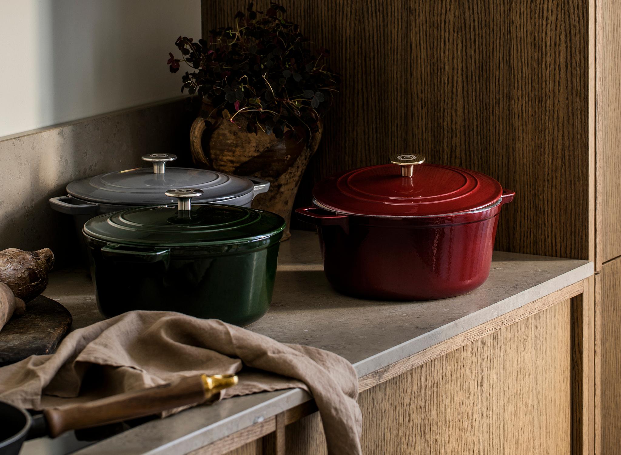 Tre röda, gröna och grå gjutjärnsgrytor på en köksbänkskiva.